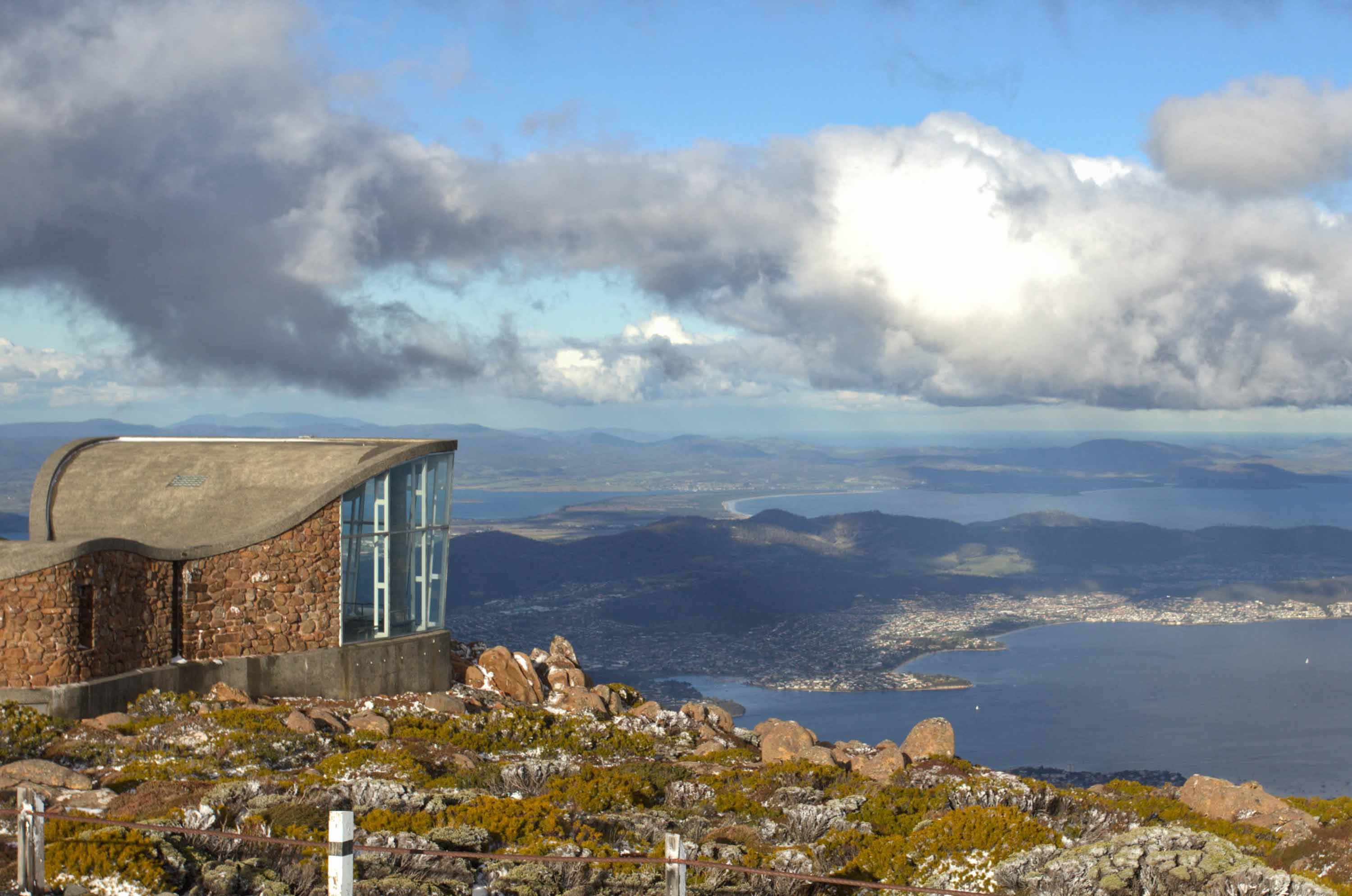 A stone building sits on the crest of a tall mountain looking down at Hobart and the Derwent River.