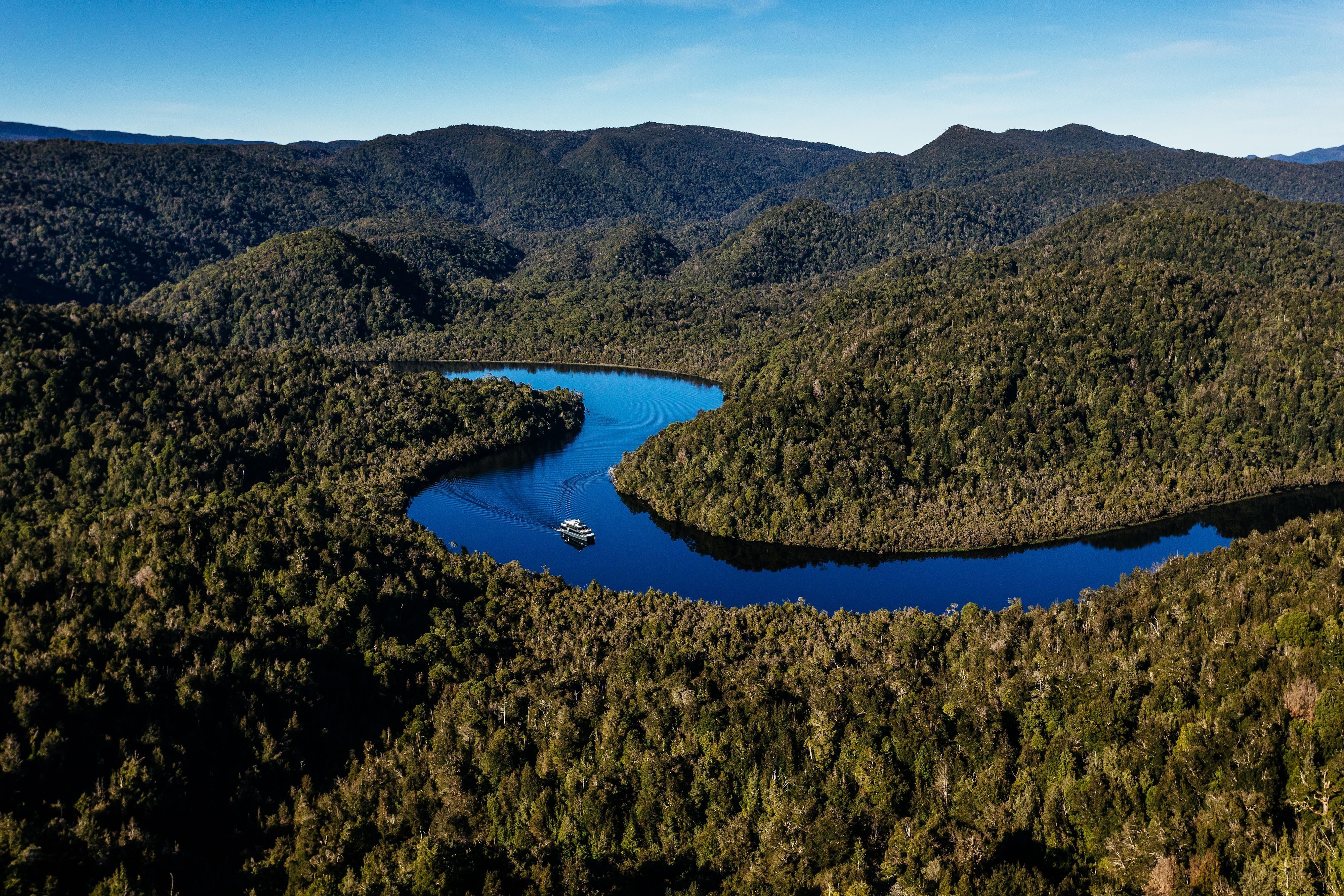 Aerial view of a cruise boat on the Gordon River winding through dense forested wilderness on Tasmania's west coast
