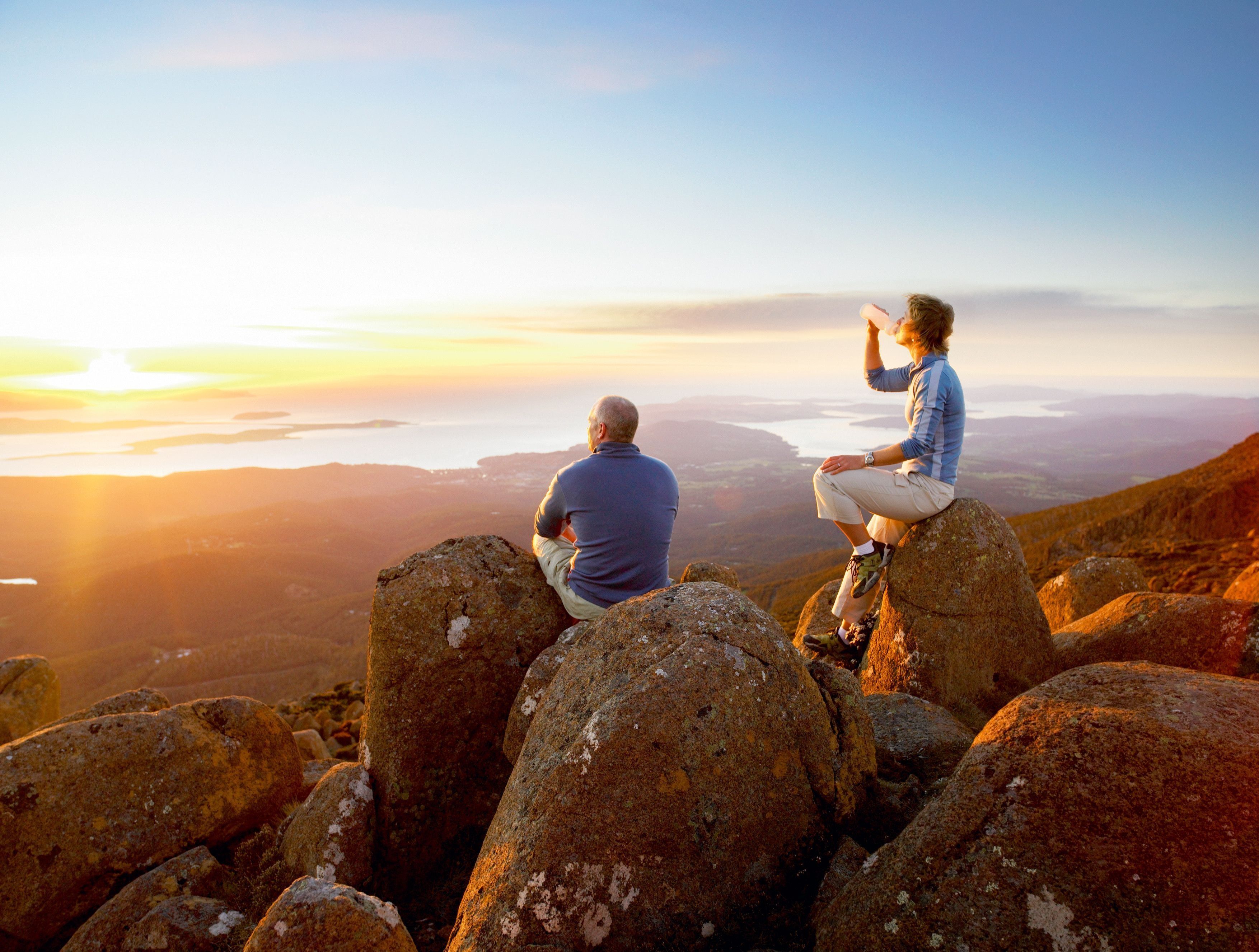 Two people resting on rocky boulders looking out over Hobart and the water from kunanyi / Mount Wellington