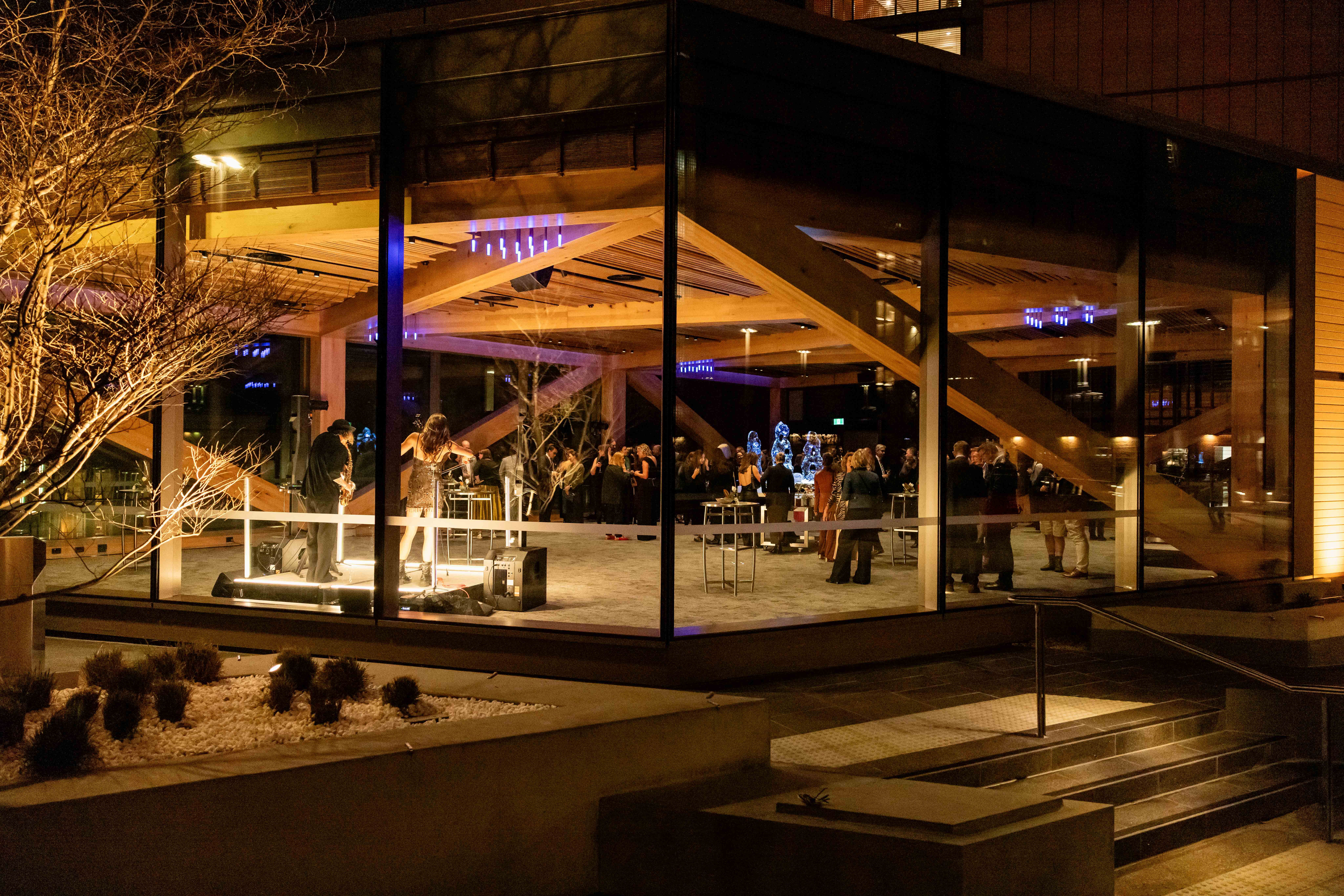 Guests mingling inside LUMINA's glass-walled event space at night, seen from outside