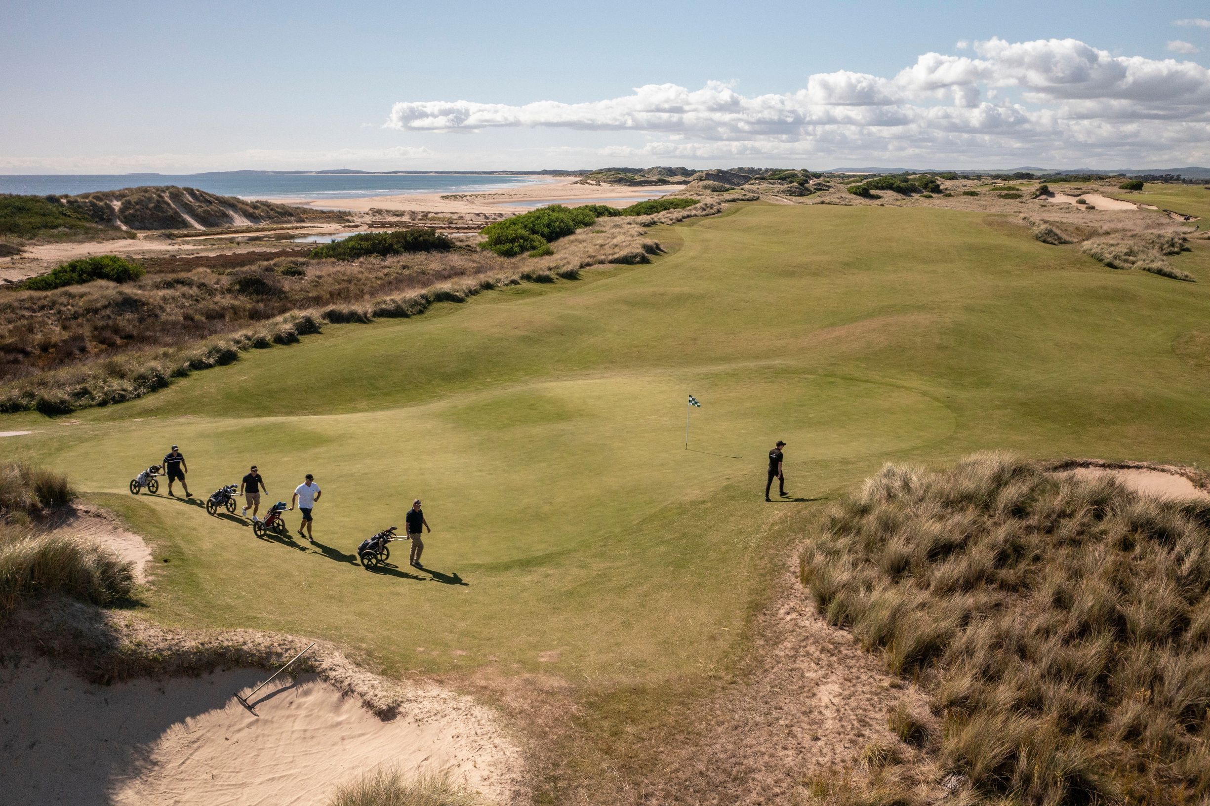 People walking toward a putting green beside coastal dunes on a Luxury Golf & Scenic Tours Tasmania outing