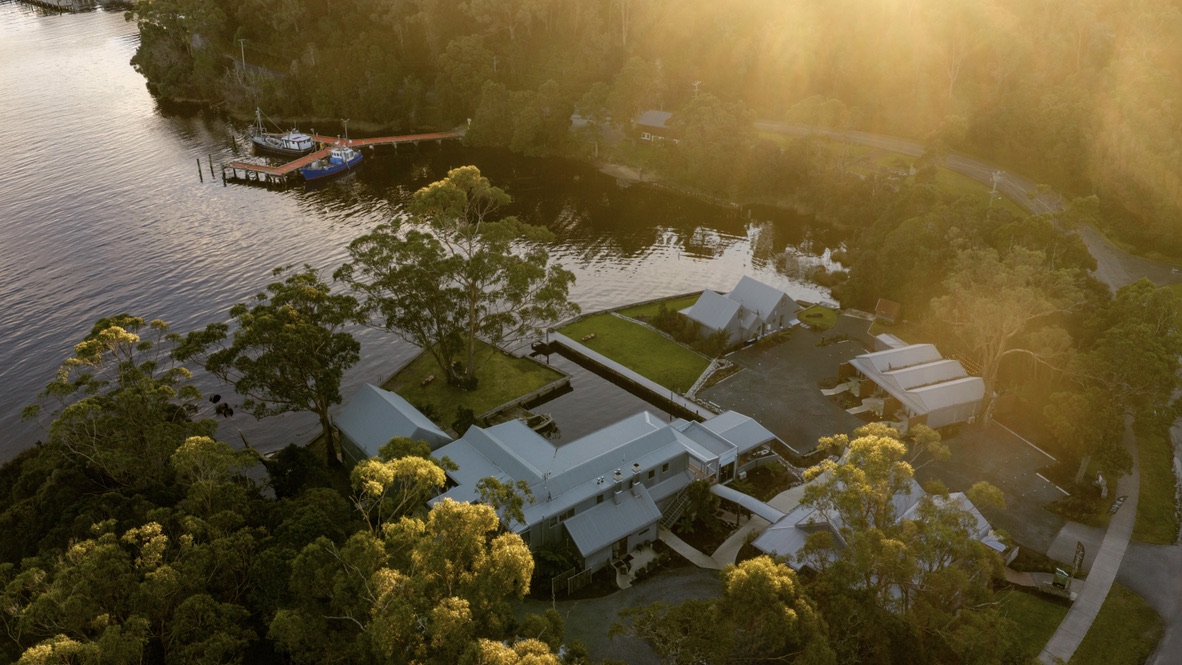 Aerial view of Risby Cove accommodation among trees beside the water at Strahan on Macquarie Harbour