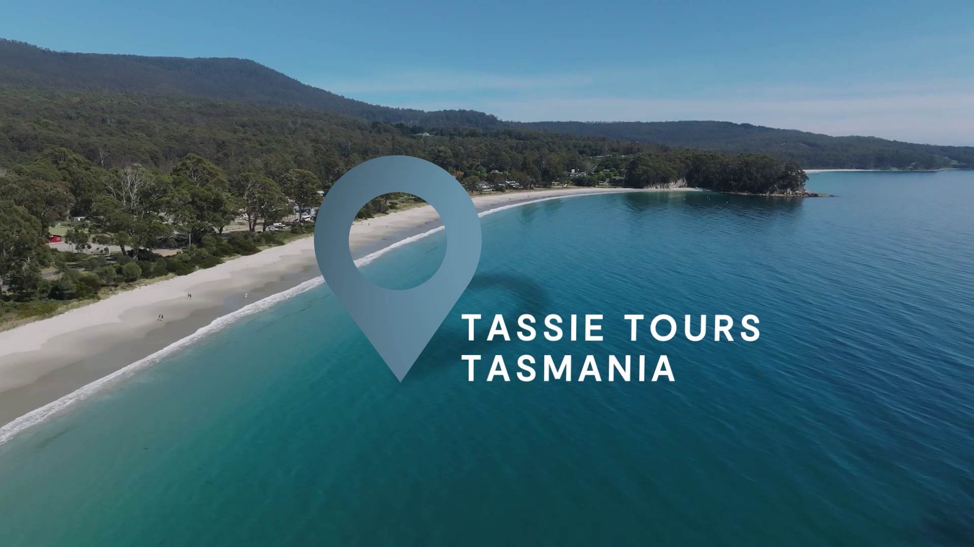 Tassie Tours Tasmania video still with a location pin over an aerial of a curved sandy beach and bay